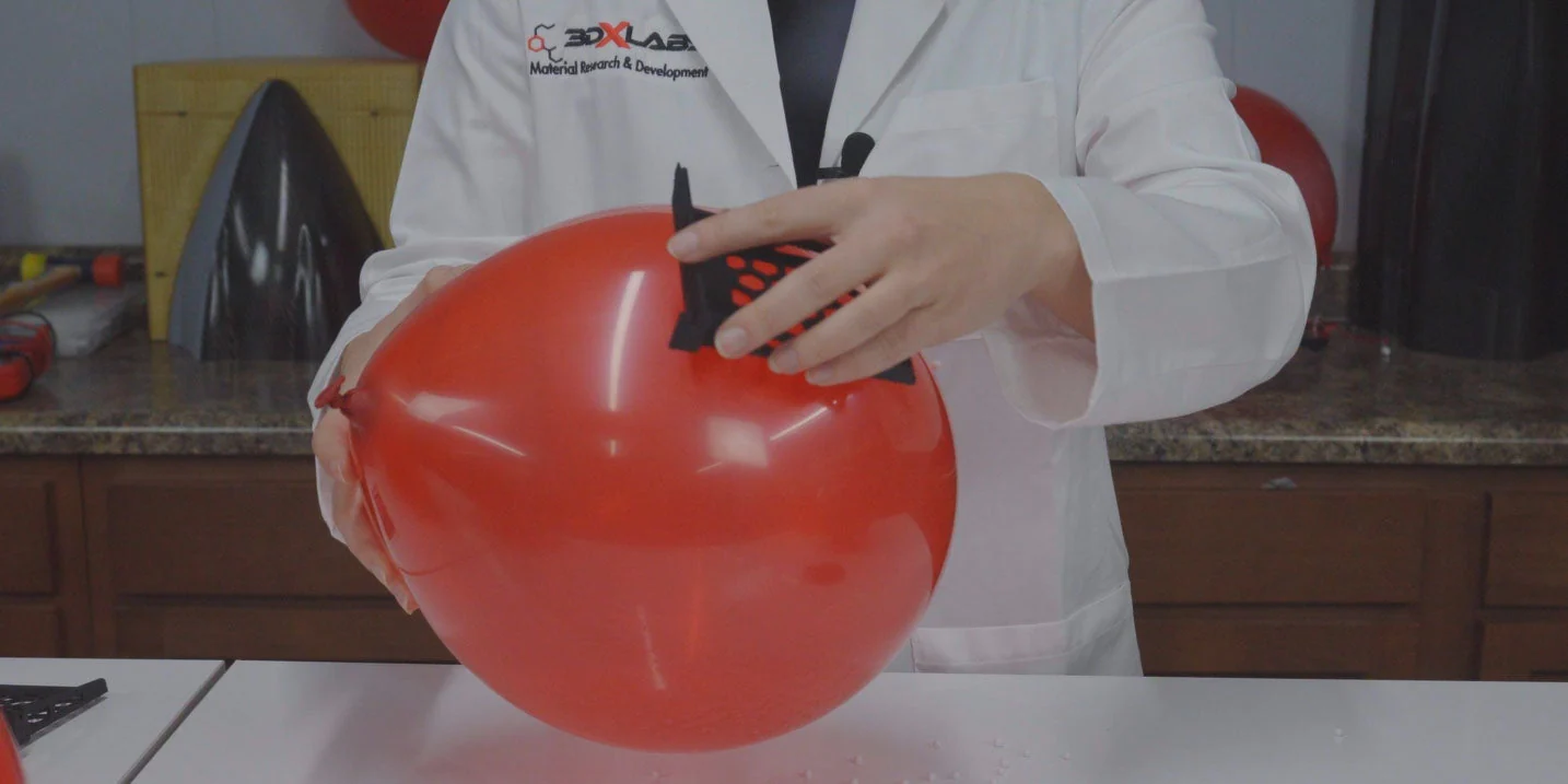 A charged balloon held against a black 3DXSTAT ESD-PLA printed part in a 3DXTech lab, showing static dissipation