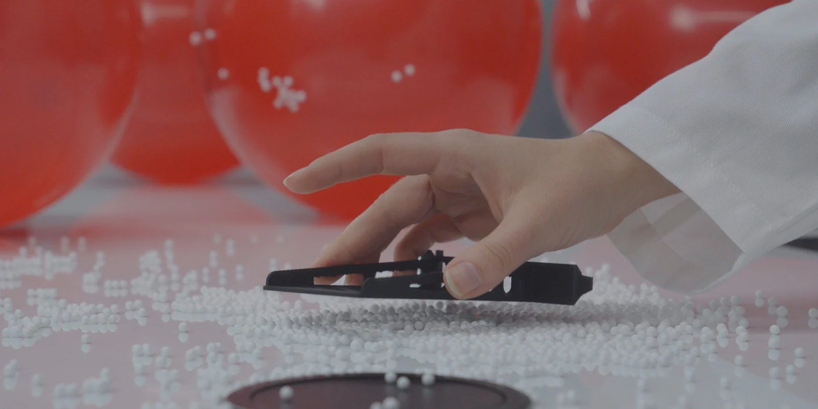 A black ESD-PLA printed bracket held over static-clinging foam beads that do not cling to the part