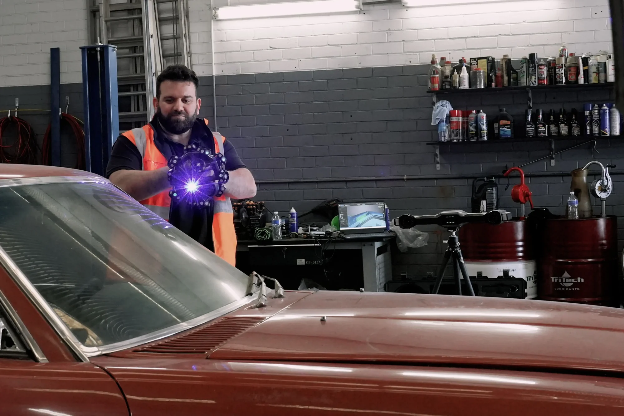 Technician scanning a classic red car in a workshop with the EinScan HX2, blue laser projection lighting the body panel