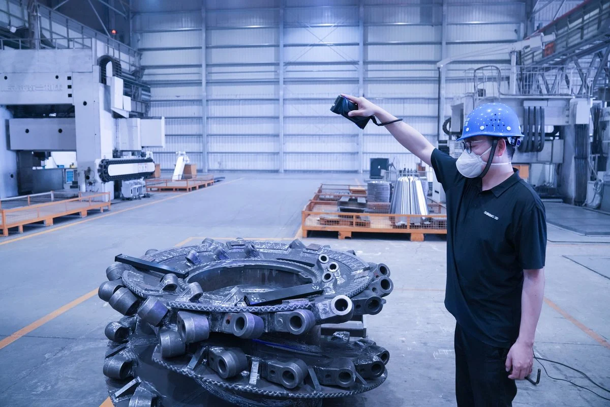 Technician in a hard hat scanning a large dark casting on a factory floor