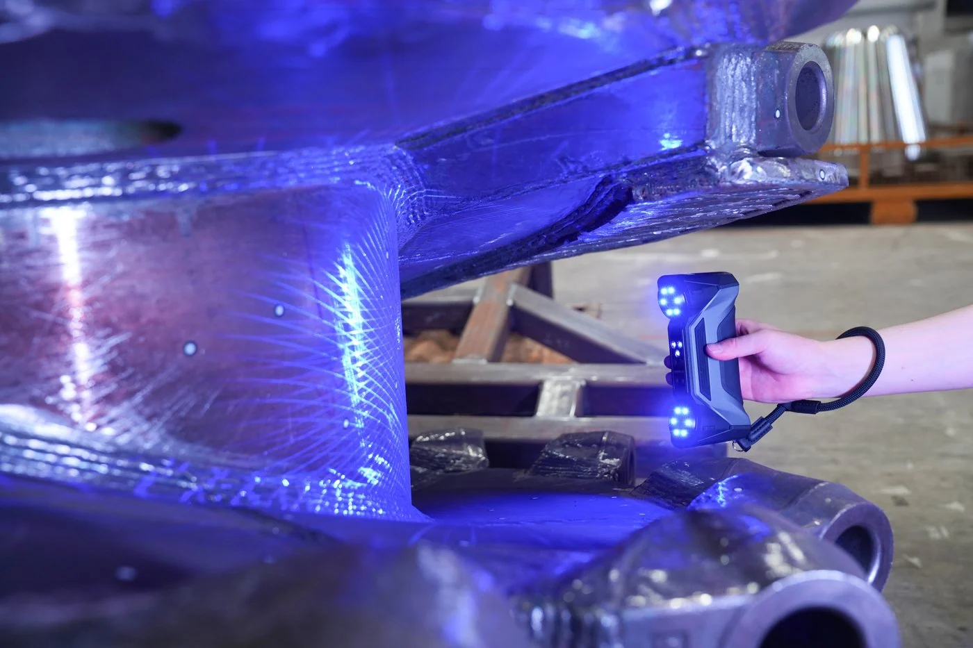 Hand holding a FreeScan Combo+ Wireless under a steel frame lit by blue laser lines