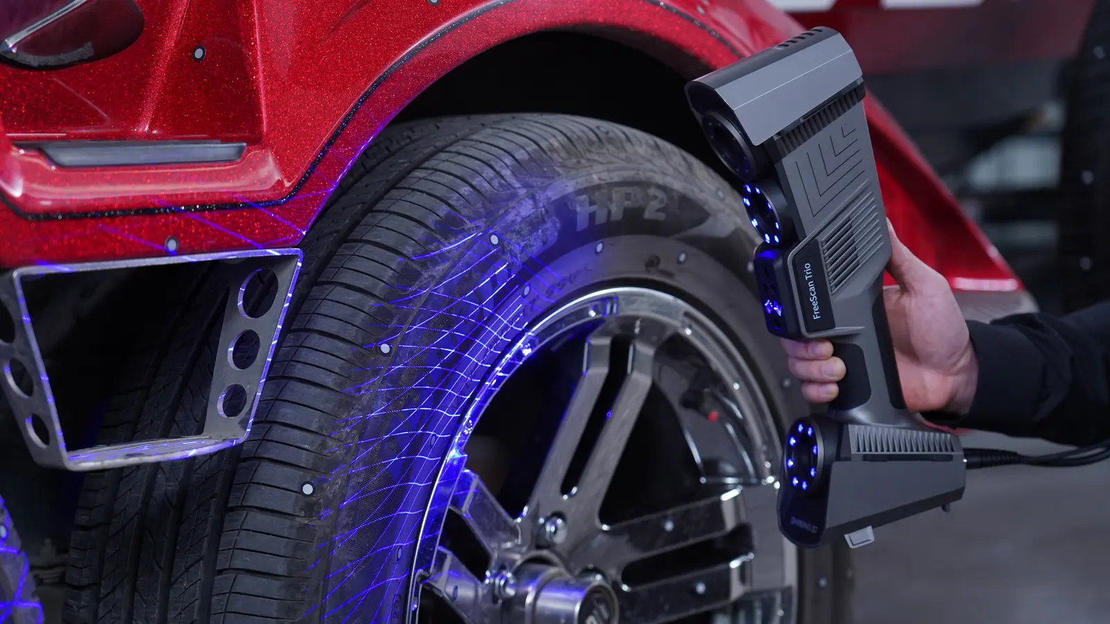 Shining 3D FreeScan Trio in Trio Blue mode — 26 blue laser lines sweeping a vehicle wheel arch at 2.7M pts/s production scan speed