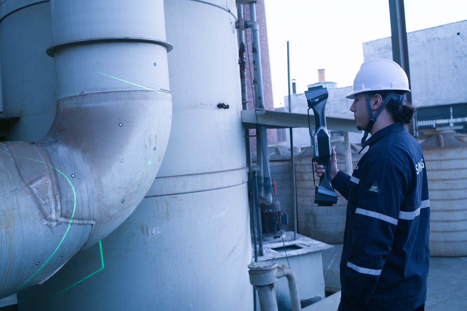 Operator scanning an industrial pipe assembly with the FreeScan UE Nova, laser cross visible on the metal surface