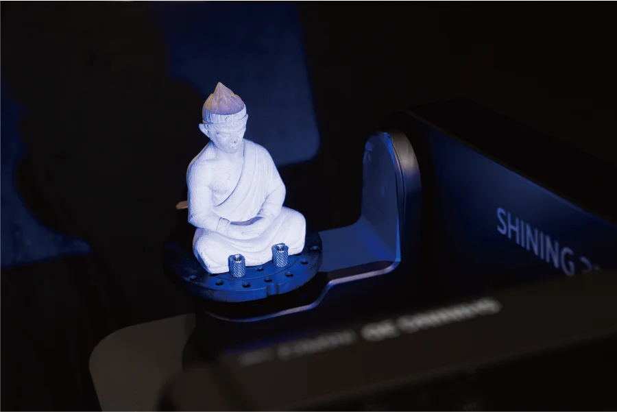 AutoScan Inspec2 capturing a Buddha statue under blue structured light &mdash; full-color 3D scan of complex organic geometry