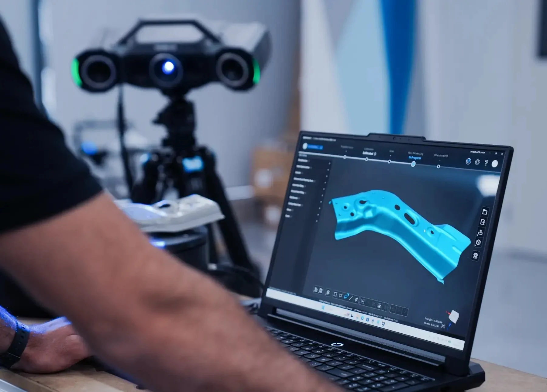 Operator at a laptop reviewing OptimScan Q12 HD scan data with the scanner fixed on its mount behind