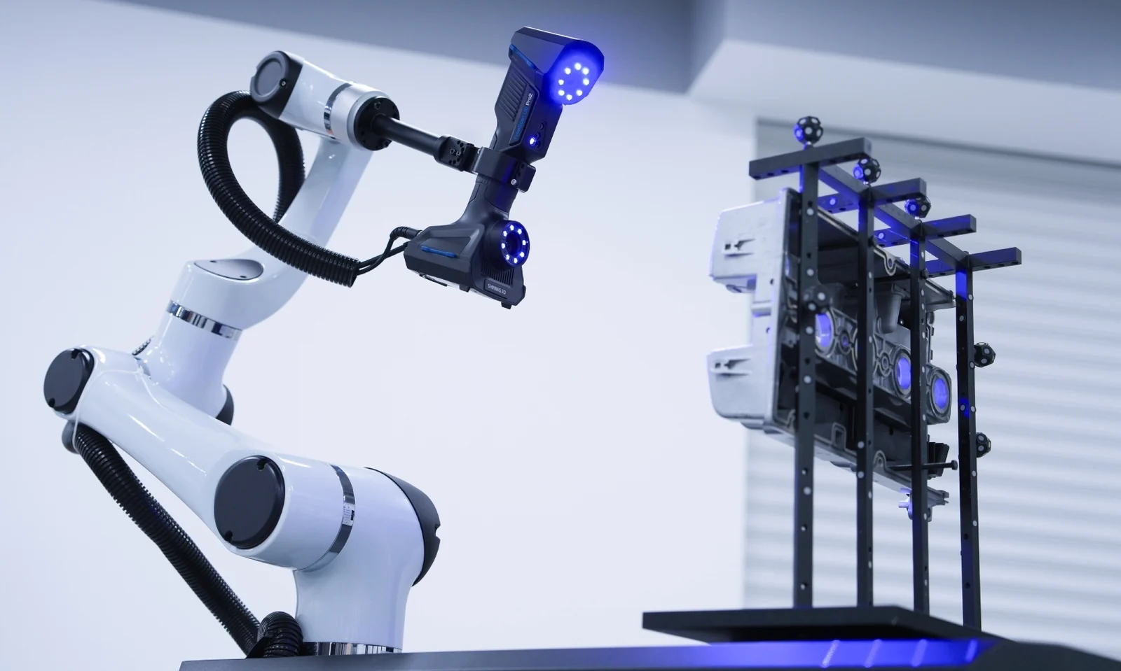 RobotScan cobot arm holding a FreeScan UE Pro2 blue-laser scanner over an engine block on a marker fixture