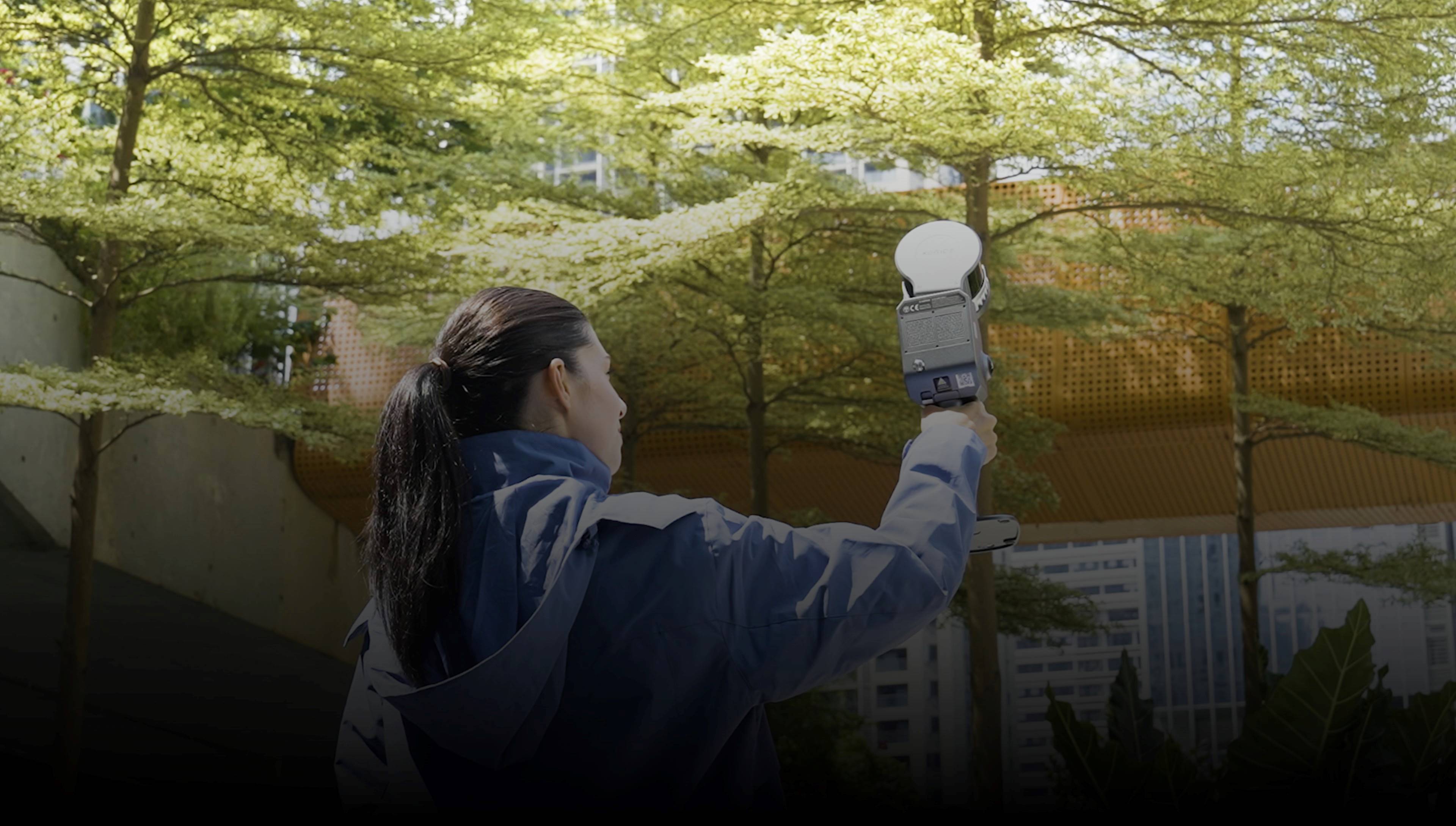 Operator capturing a tree-lined urban park handheld with the XGRIDS Lixel L2 Pro and live LixelGo preview